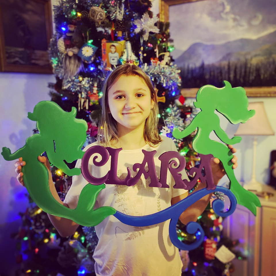 Girl Poses with Baby Name Sign in front of Christmas tree