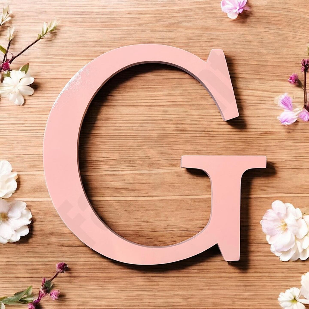 Pink letter 'G' on a wooden surface with flowers around