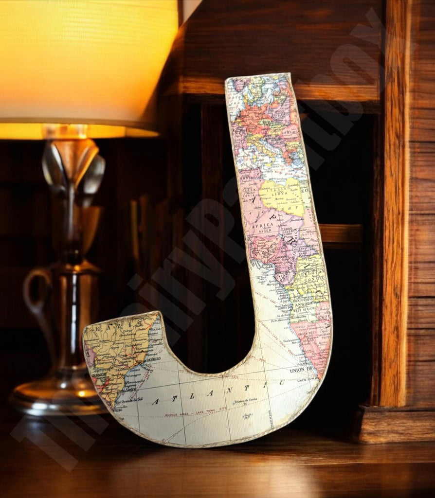 Decorative letter 'U' with world map design on a wooden surface next to a lamp.