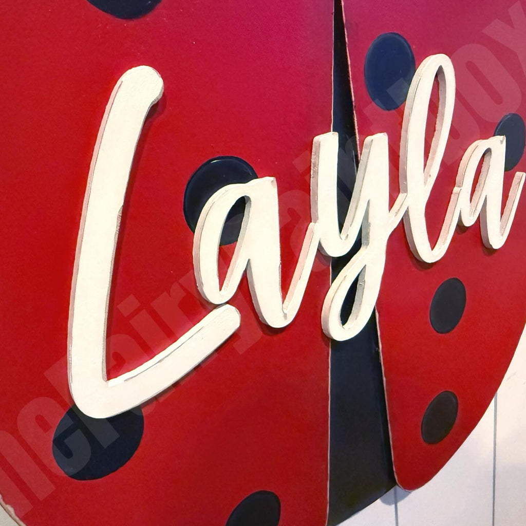 Red ladybug-shaped sign with 'Layla' in white cursive text