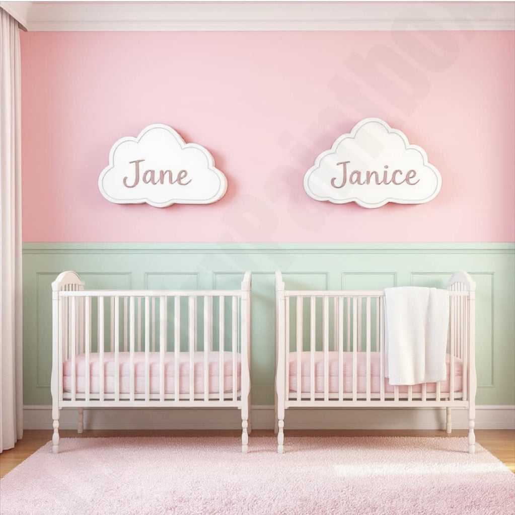 Nursery room with two cribs and cloud-shaped wall decorations with names on a pink and green wall.