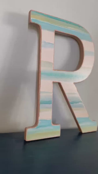 Coastal Hues Blue and Green painted monogram letter that sits on a blue desk.