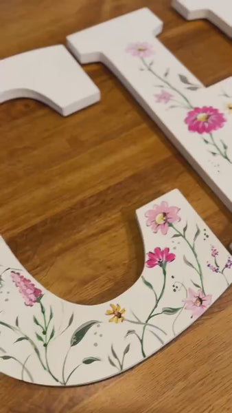 White wooden letters painted with flowers spelling a baby's name.